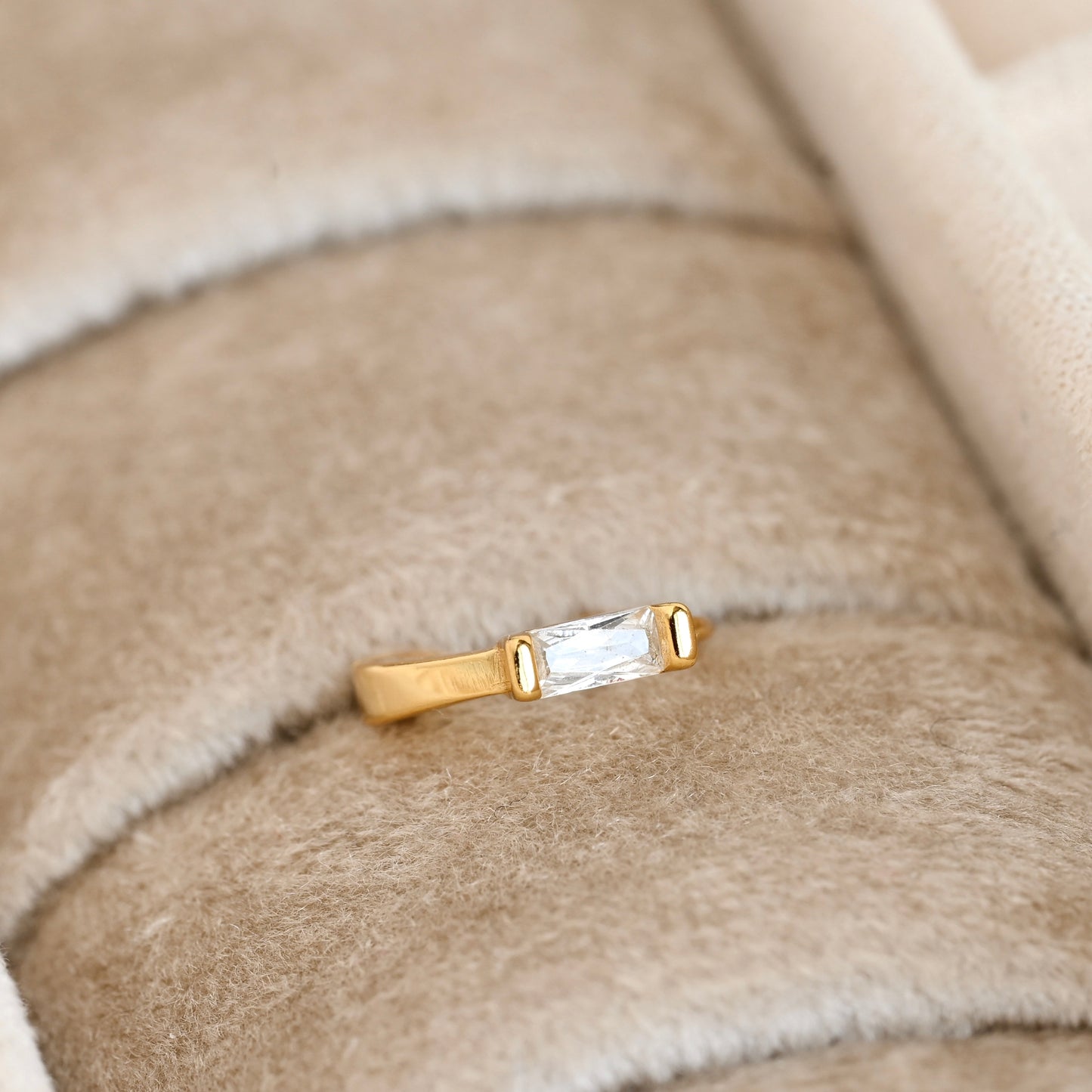 Gold huggie earring with a clear baguette gemstone on a beige fabric background