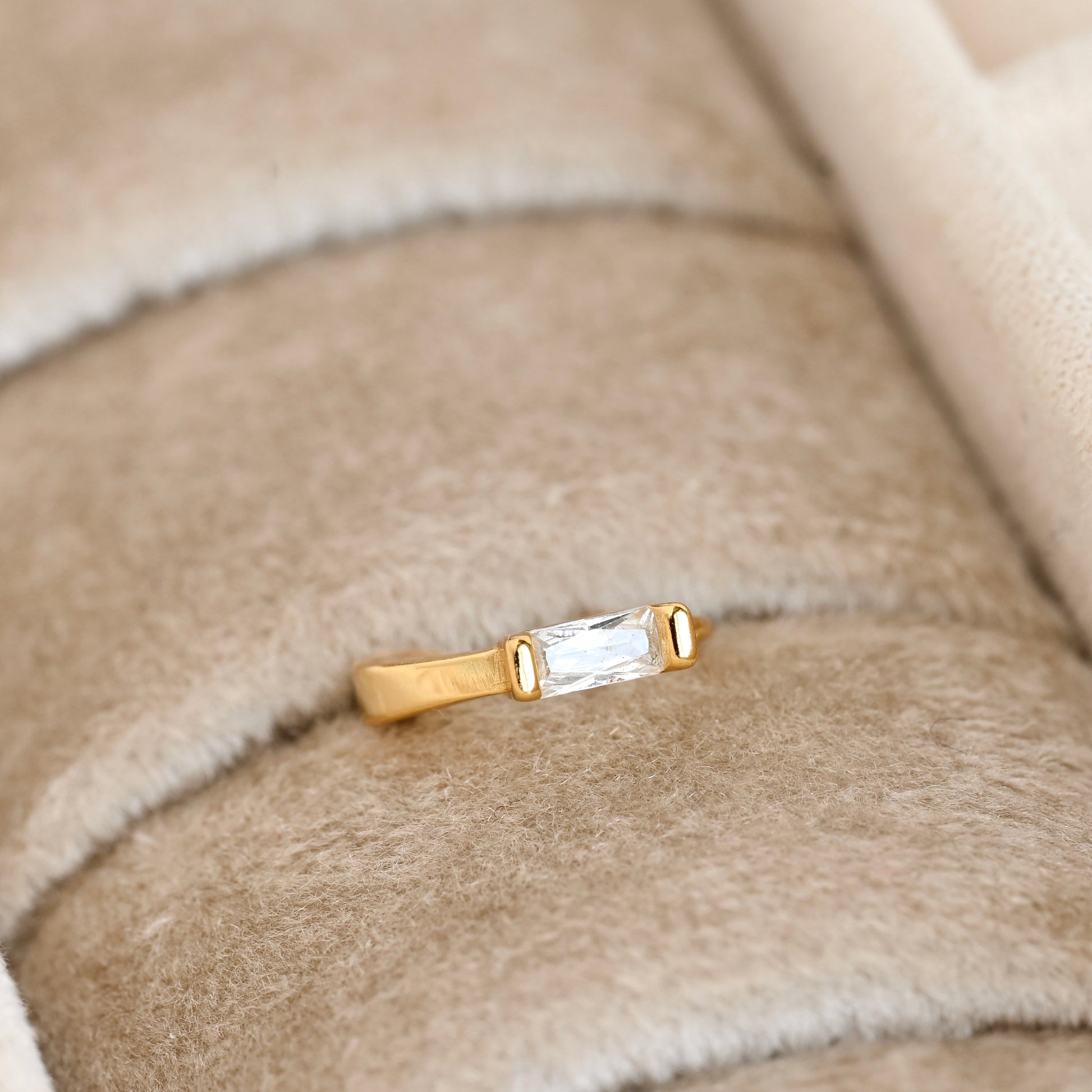 Gold huggie earring with a clear baguette gemstone on a beige fabric background