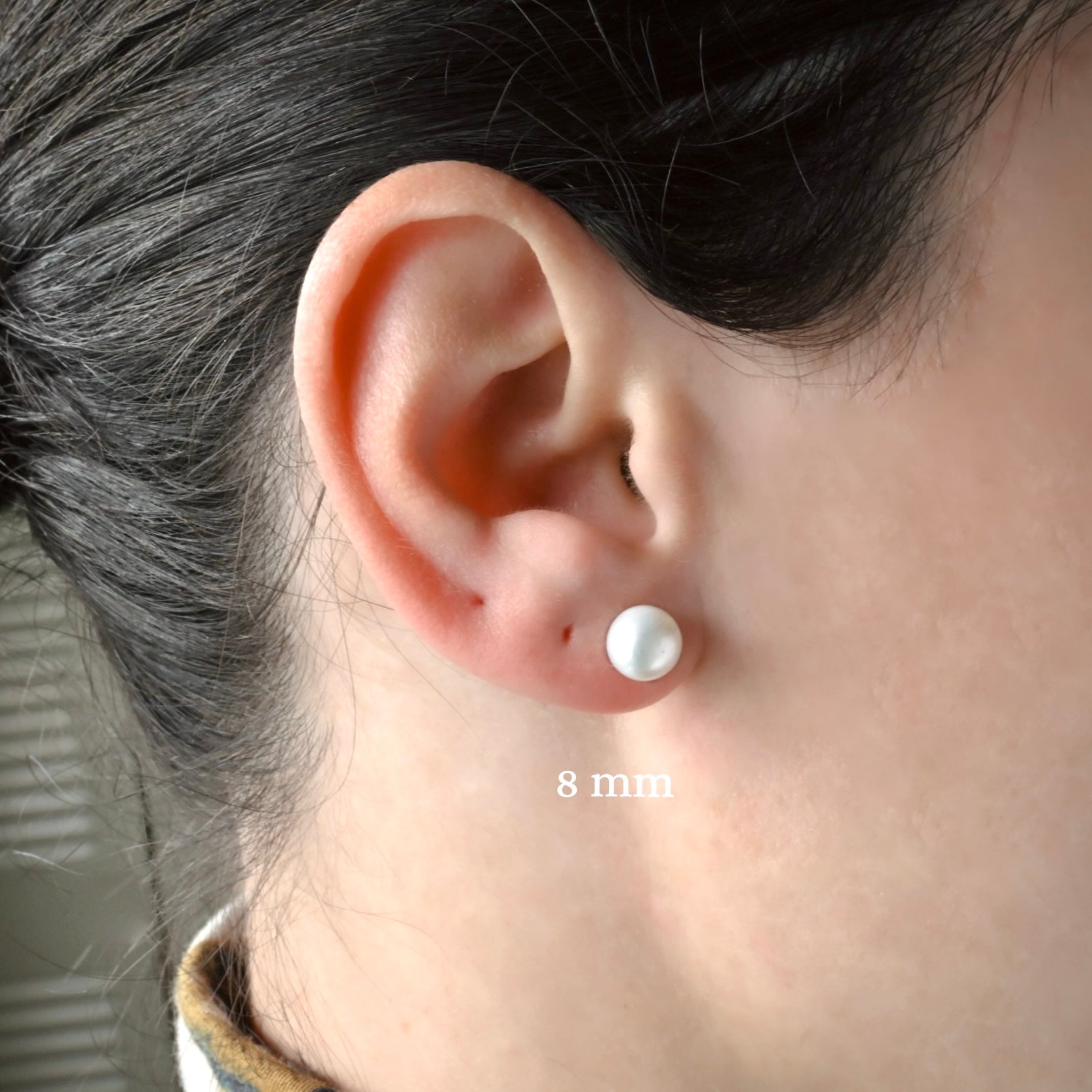 Close-up of an ear wearing a medium sized white pearl earring with '8 mm' label.
