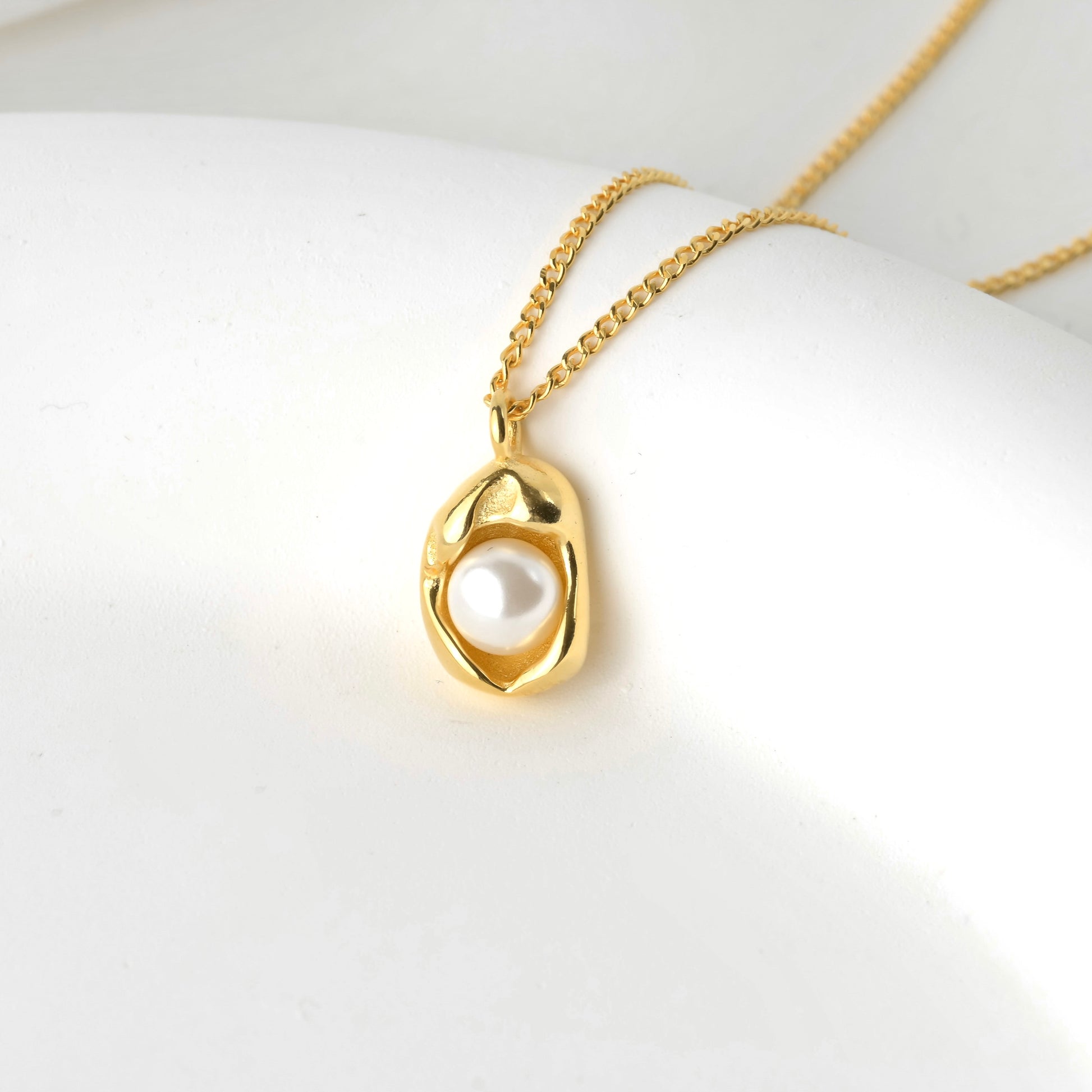 Gold necklace with a pendant featuring an oyster shell holding a white pearl.