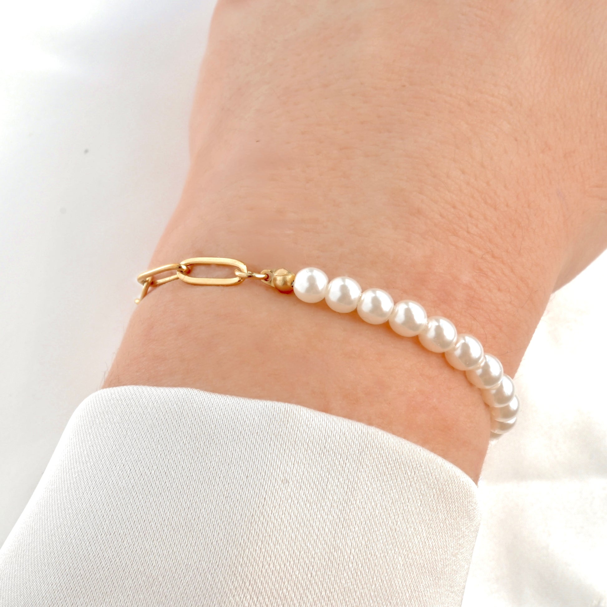 Half pearl half paperclip bracelet on a wrist with a gold toggle clasp against a white background