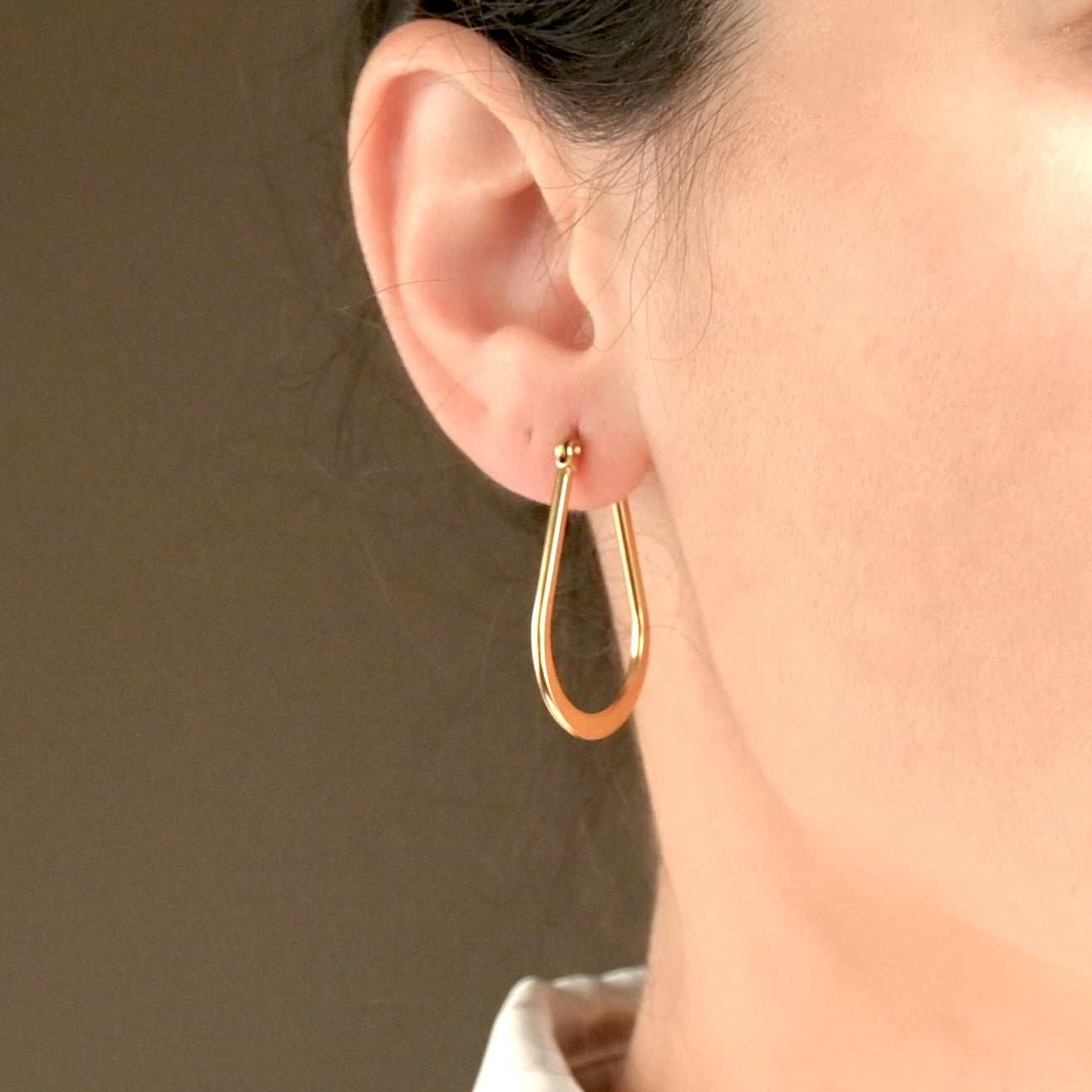 Front view of gold teardrop oultine hoop earrings worn by a person against a neutral background