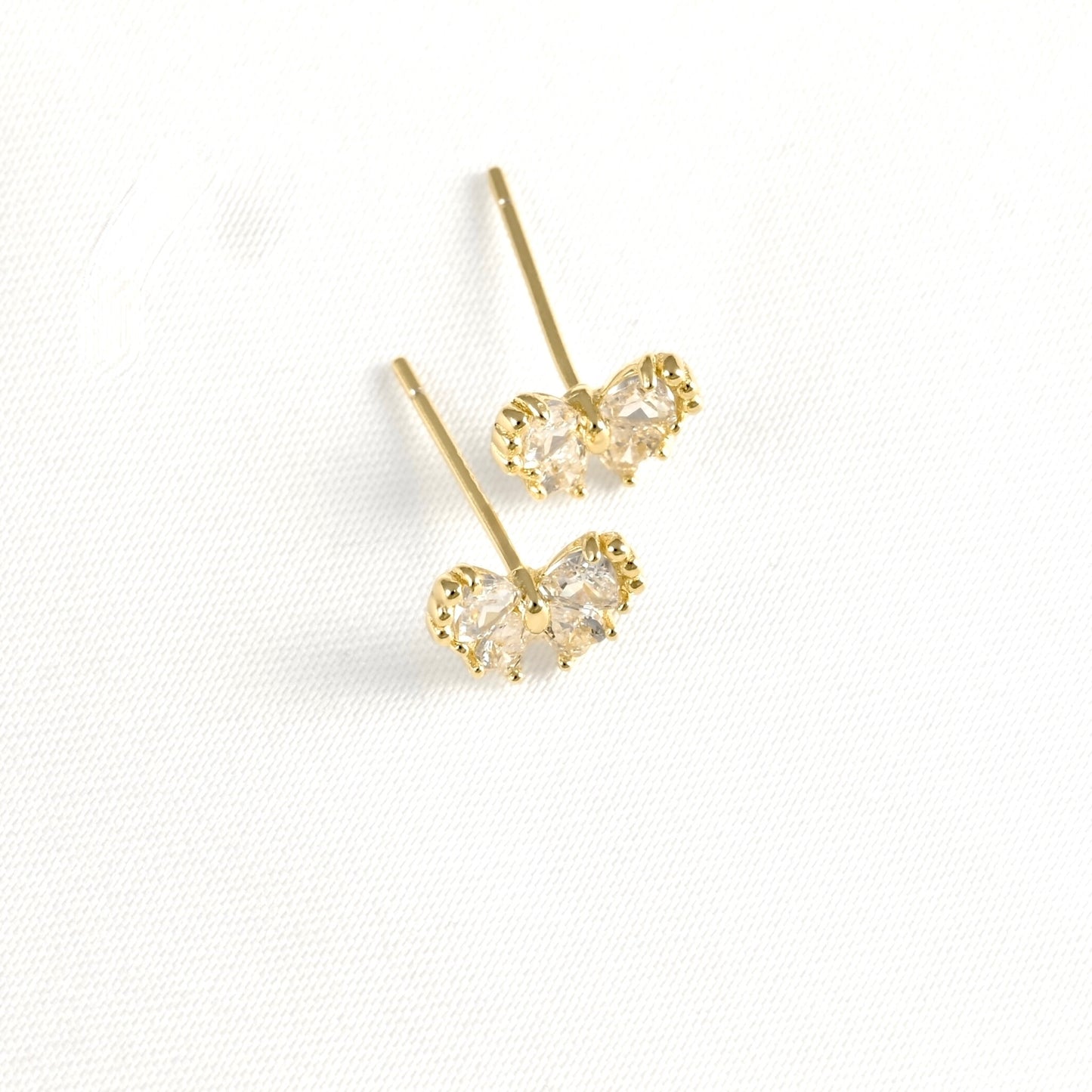 Top view of a pair of gold butterfly stud earrings with clear gemstones, displayed on a textured white fabric background.