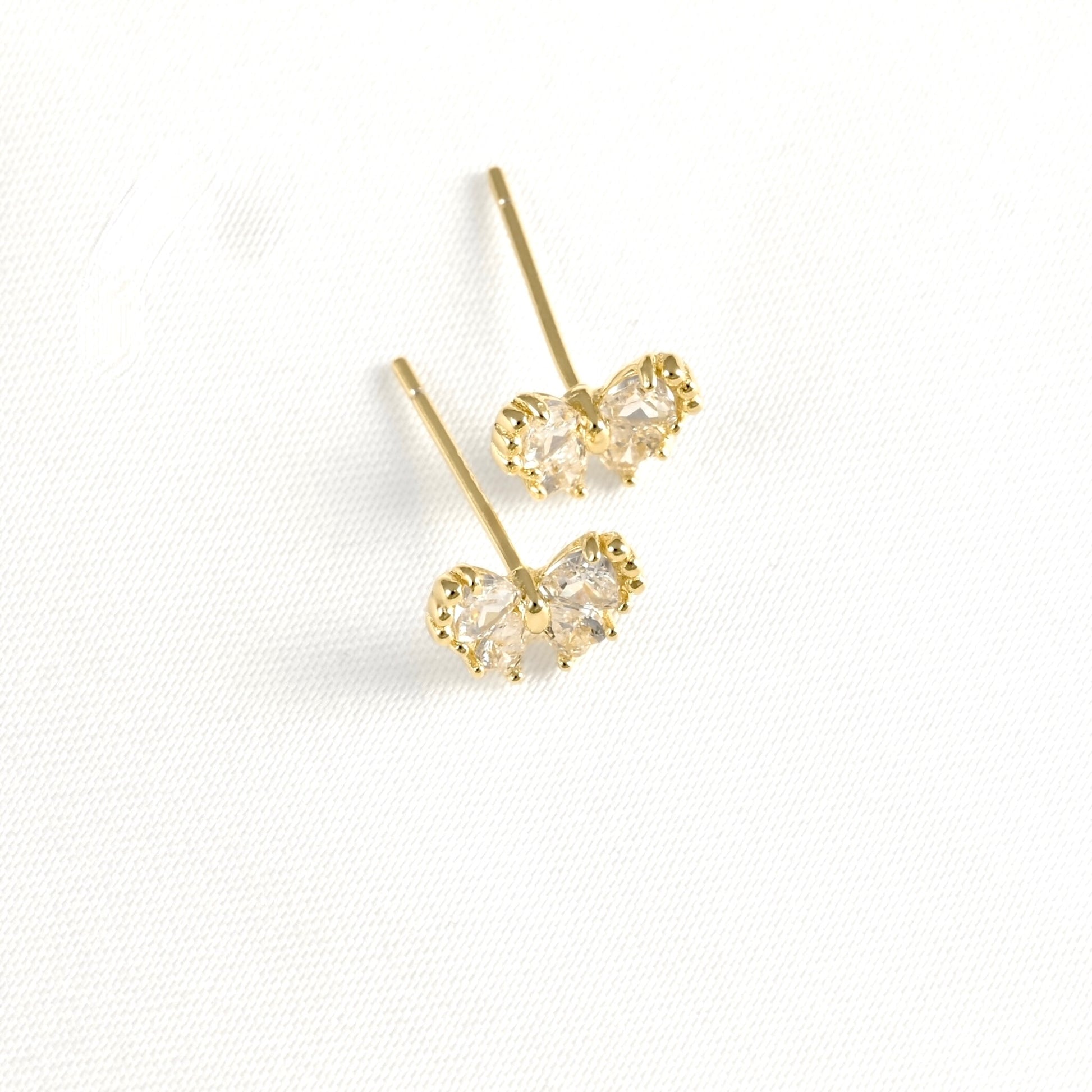 Top view of a pair of gold butterfly stud earrings with clear gemstones, displayed on a textured white fabric background.