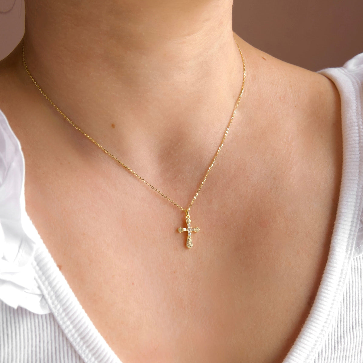 Gold necklace with a cross pendant worn by a person in a white blouse.