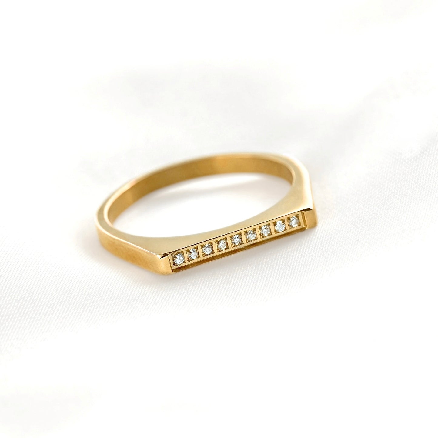 A gold signet-style ring with a row of small clear stones set across the top, photographed on a soft white fabric background.