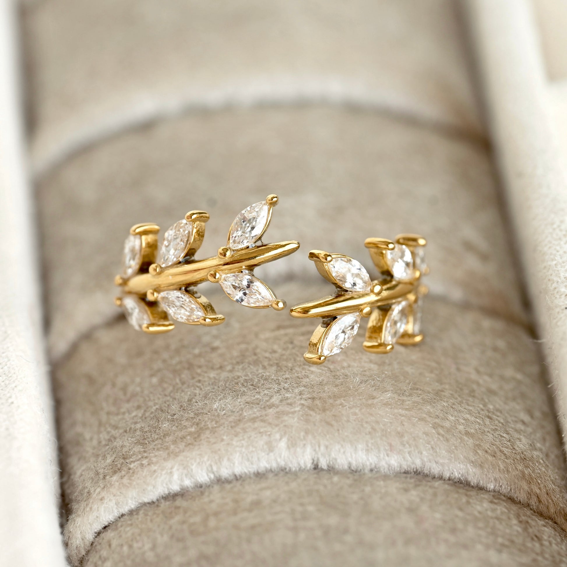 A gold leaf-shaped ring with marquise-cut clear stones, displayed on a beige velvet ring box.