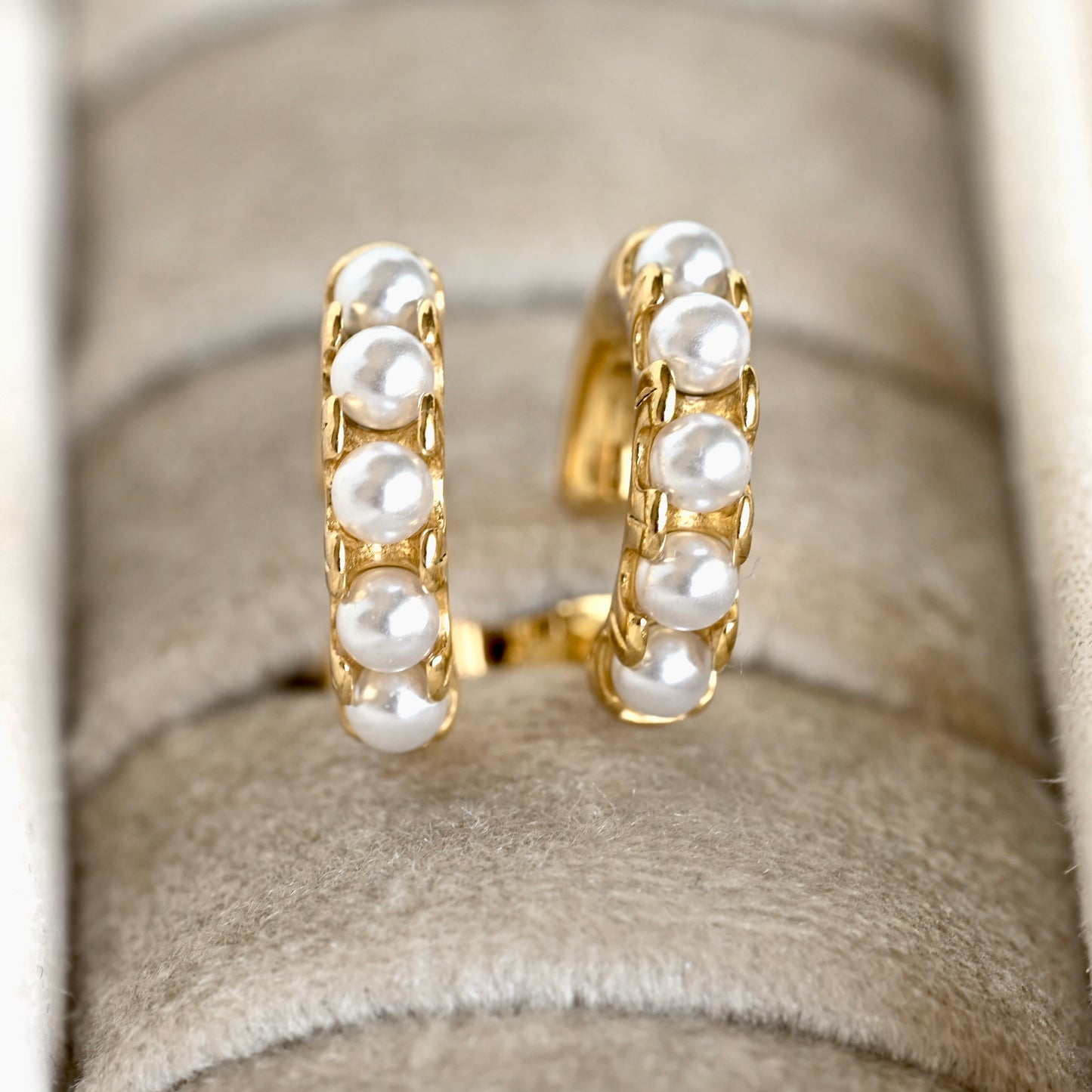 A pair of gold hoop earrings with five white pearl-like beads set vertically on each hoop, displayed on a beige velvet jewelry ring stand.