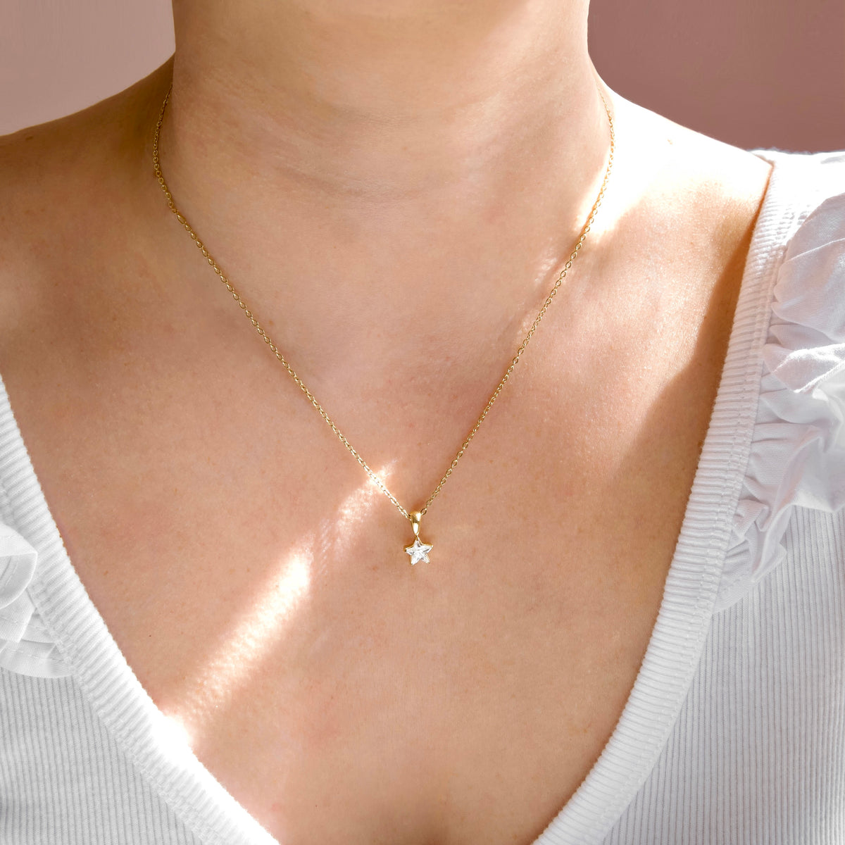 A delicate gold chain necklace with a small star-shaped pendant worn by a model. The necklace is shown against the model's neck and upper chest, wearing a white ribbed top.