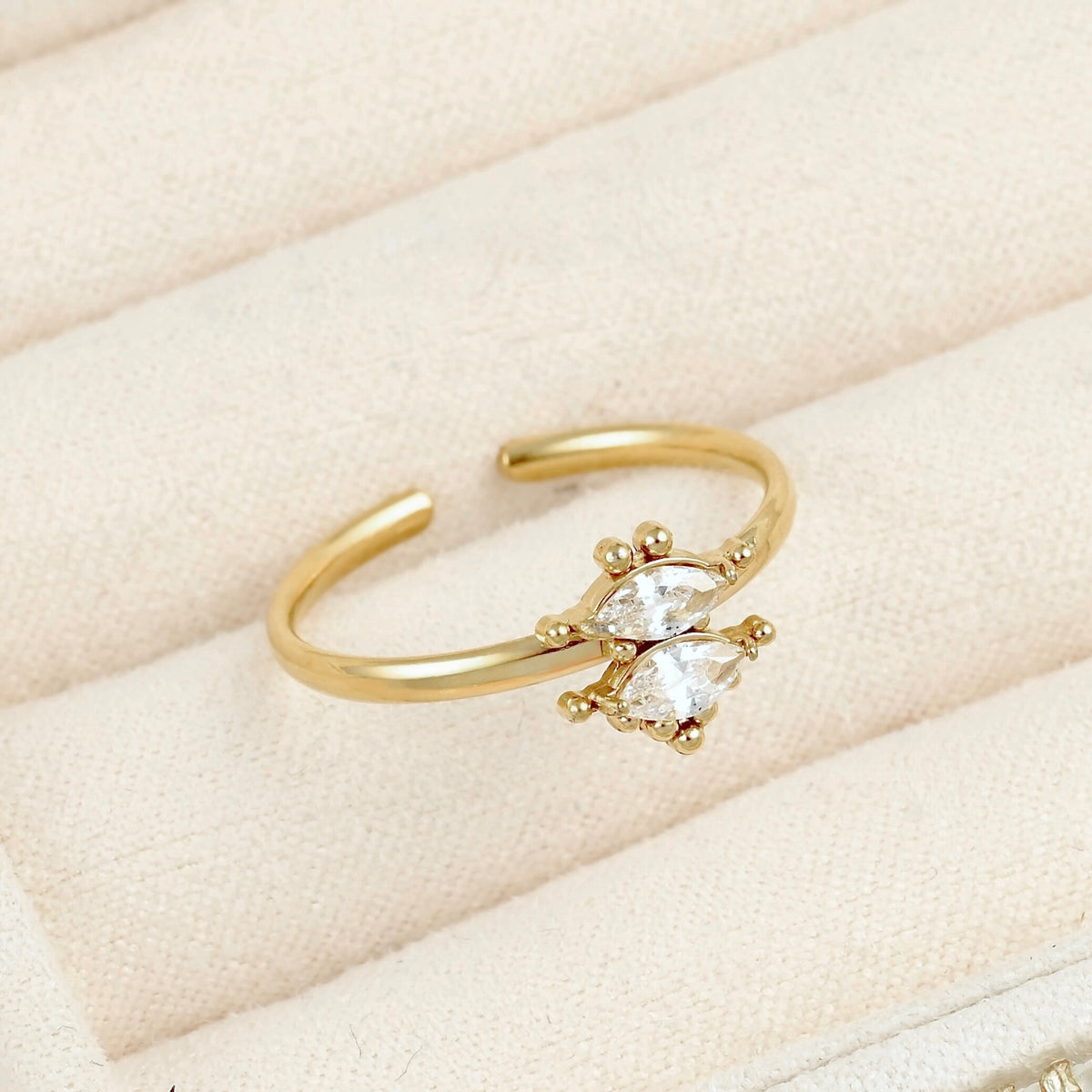 A gold adjustable ring with a butterfly-shaped clear gemstone, displayed on a cream-colored textured jewelry box.