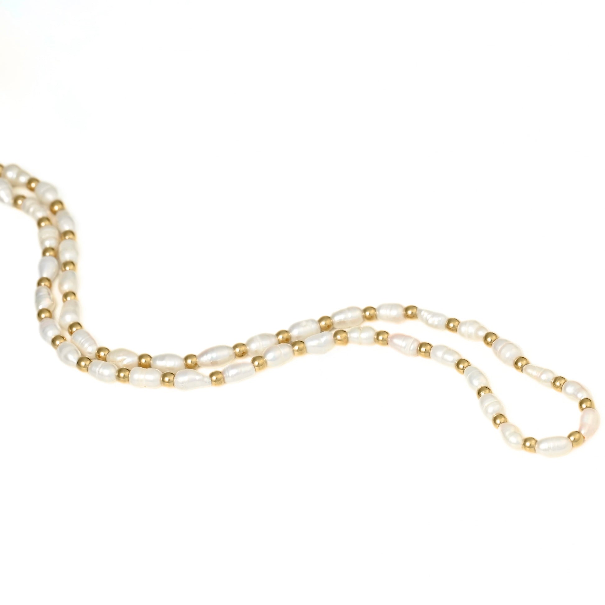 A gold pearl necklace featuring white baroque pearls and small stainless steel gold spacer beads, laid out on a plain white background.