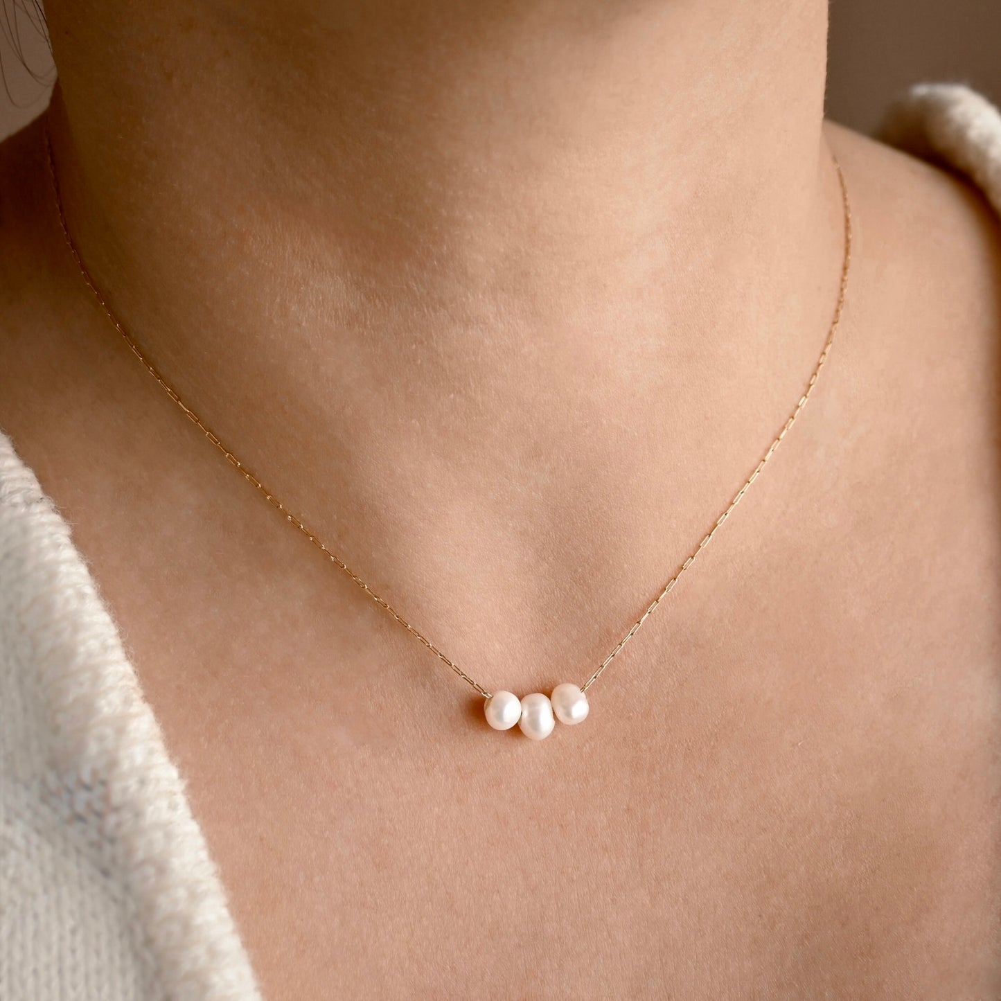 A delicate gold pearl necklace with three small, lustrous white pearls at the center, worn on a model's neck.