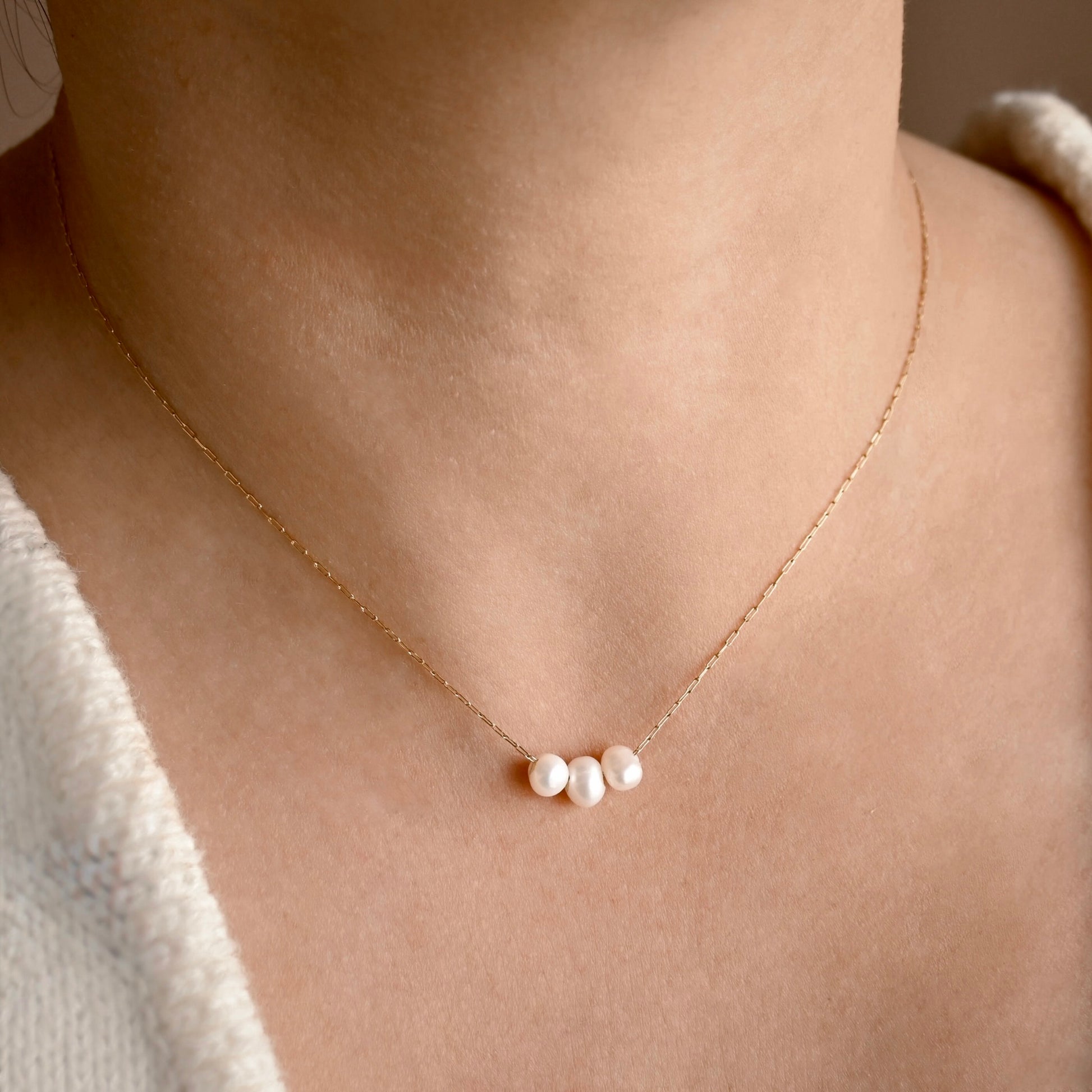A delicate gold pearl necklace with three small, lustrous white pearls at the center, worn on a model's neck.