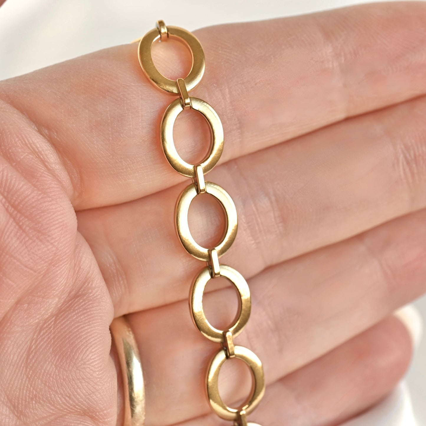 A close-up of a gold link chain bracelet resting on a person's hand, showing the polished oval links and metal finish.