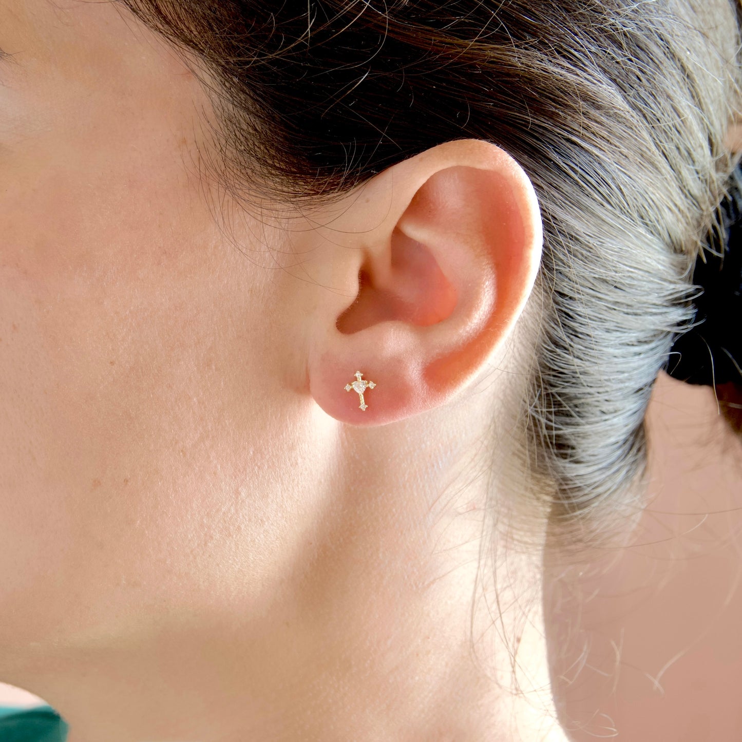 A close-up of a person's ear wearing a small gold cross stud earring.