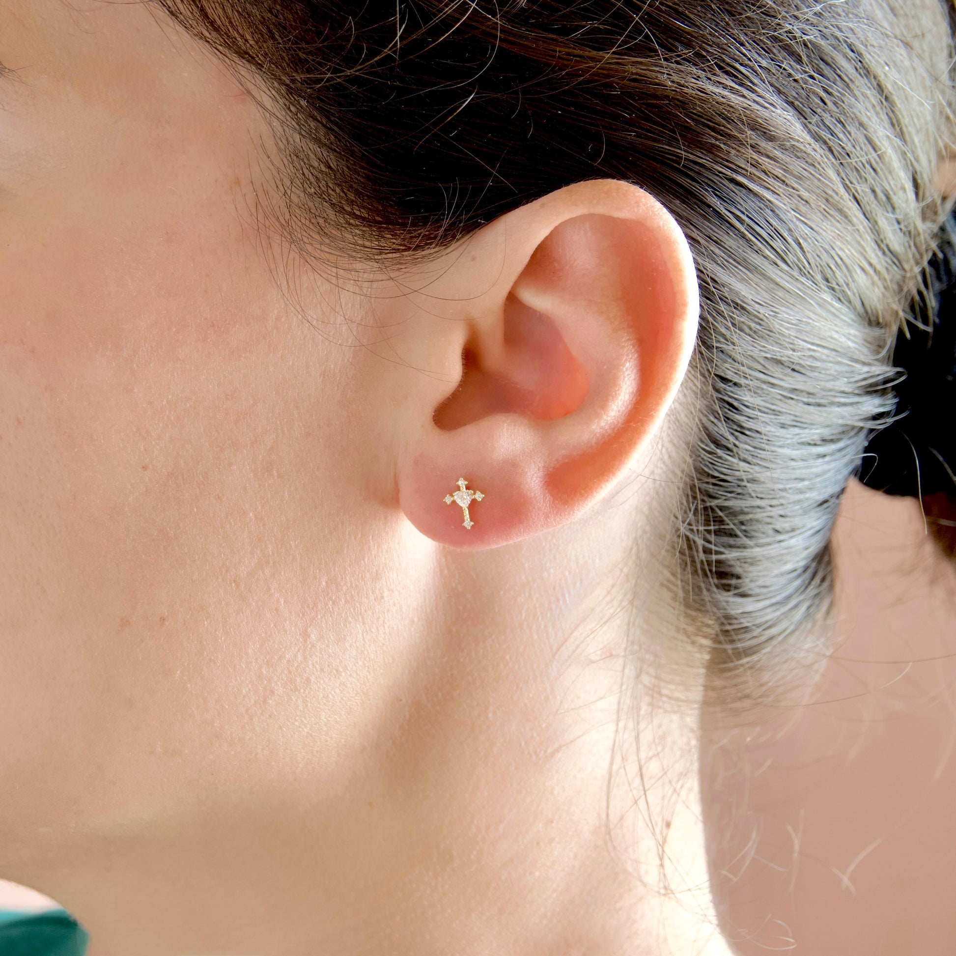 A close-up of a person's ear wearing a small gold cross stud earring.