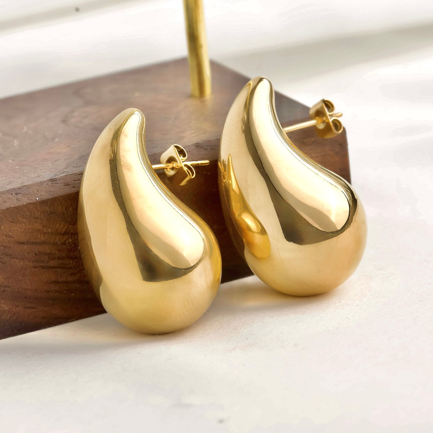 Gold designer earrings on a wooden stand with a white background