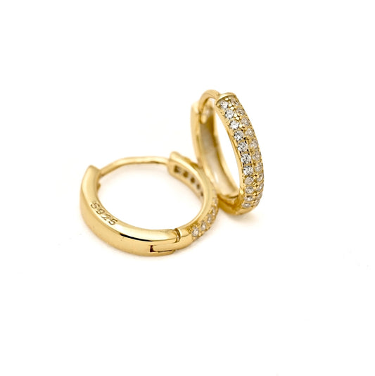 A pair of gold huggie hoop earrings with pavé-set clear stones on one side, shown on a plain white background. One earring is open to reveal the hinge and a '925' sterling silver hallmark stamped on the inside.