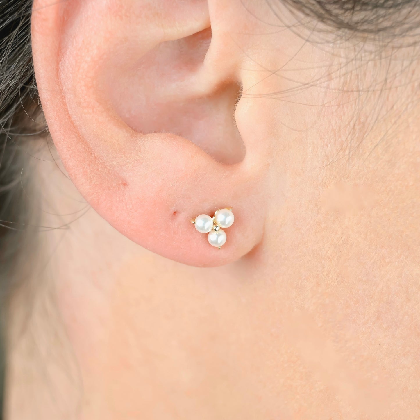 Close-up of an ear wearing a gold earring with pearls.