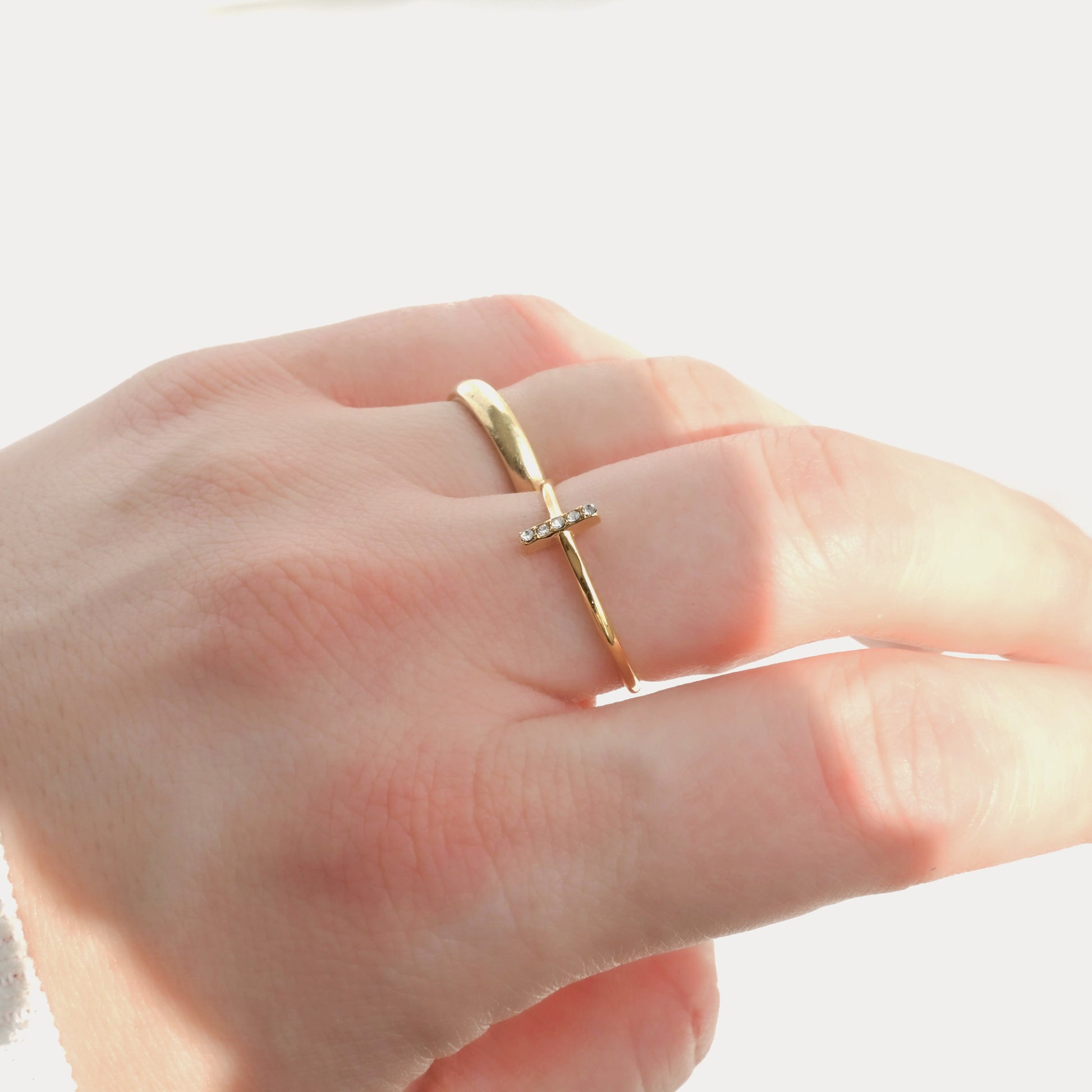 Gold ring with a cross design on a person's finger against a white background