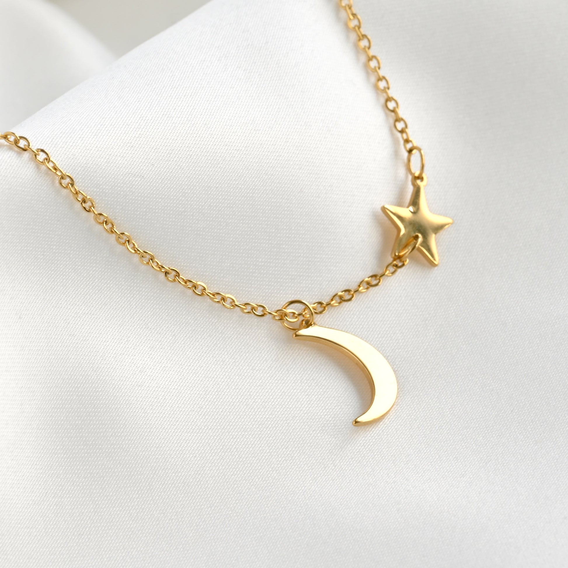 Gold necklace with a star charm and crescent moon pendant on a white background