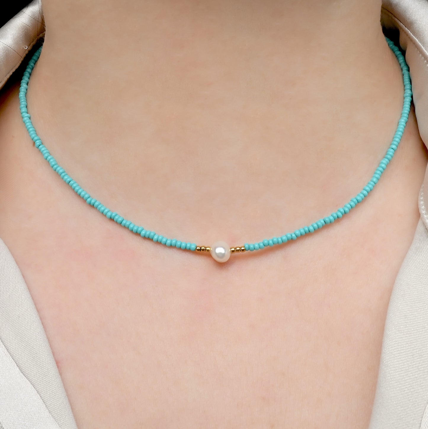 Front view of turquoise beaded necklace with a pearl pendant on a person wearing a white shirt.