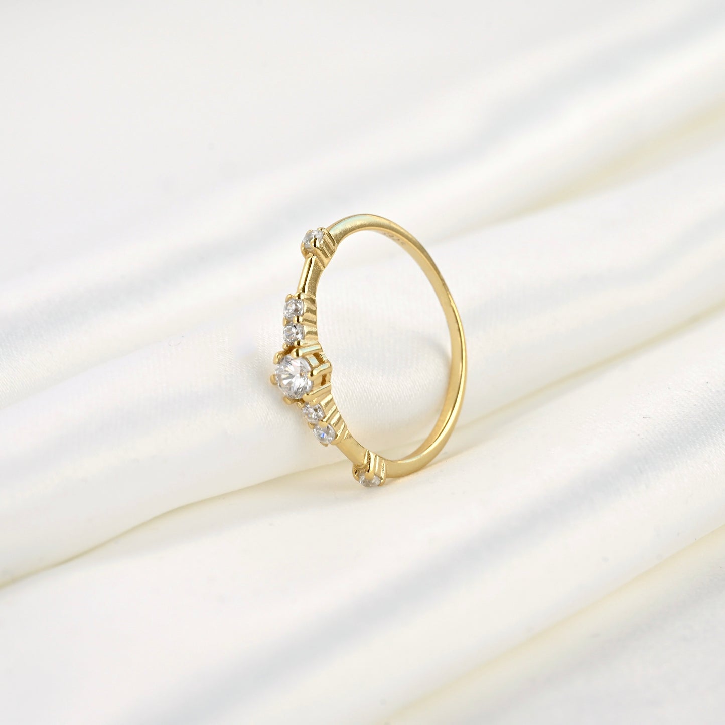 Gold ring with diamonds standing  against folded white satin fabric.