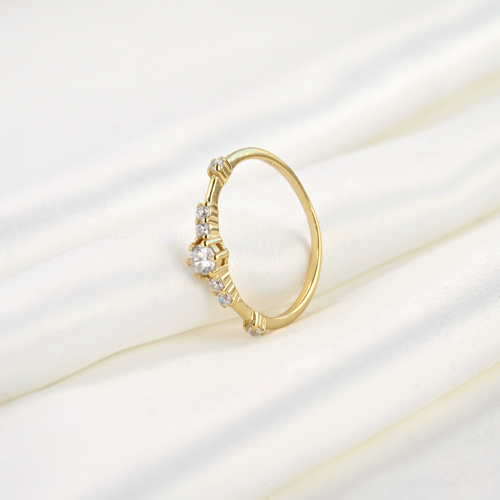 Gold ring with diamonds standing  against folded white satin fabric.