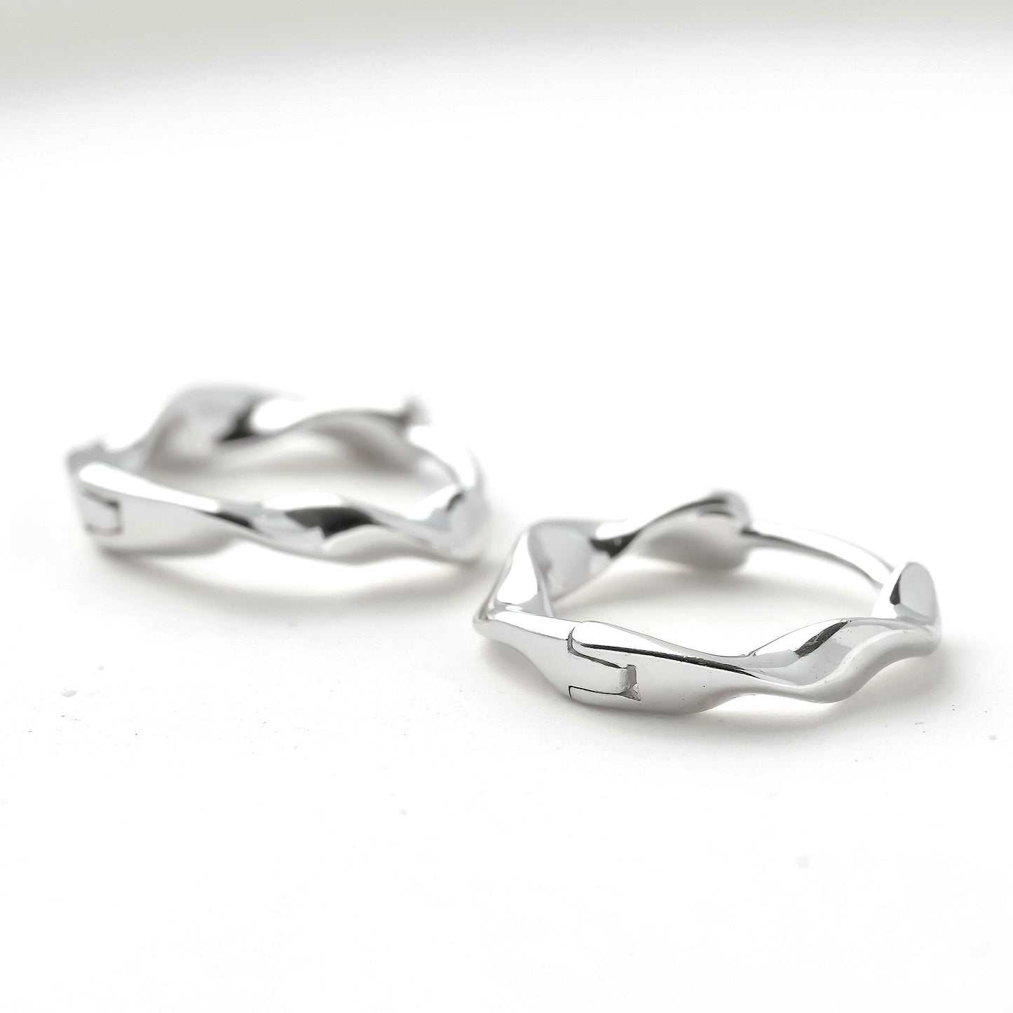Pair of silver huggie earrings with hinged closure on a white background