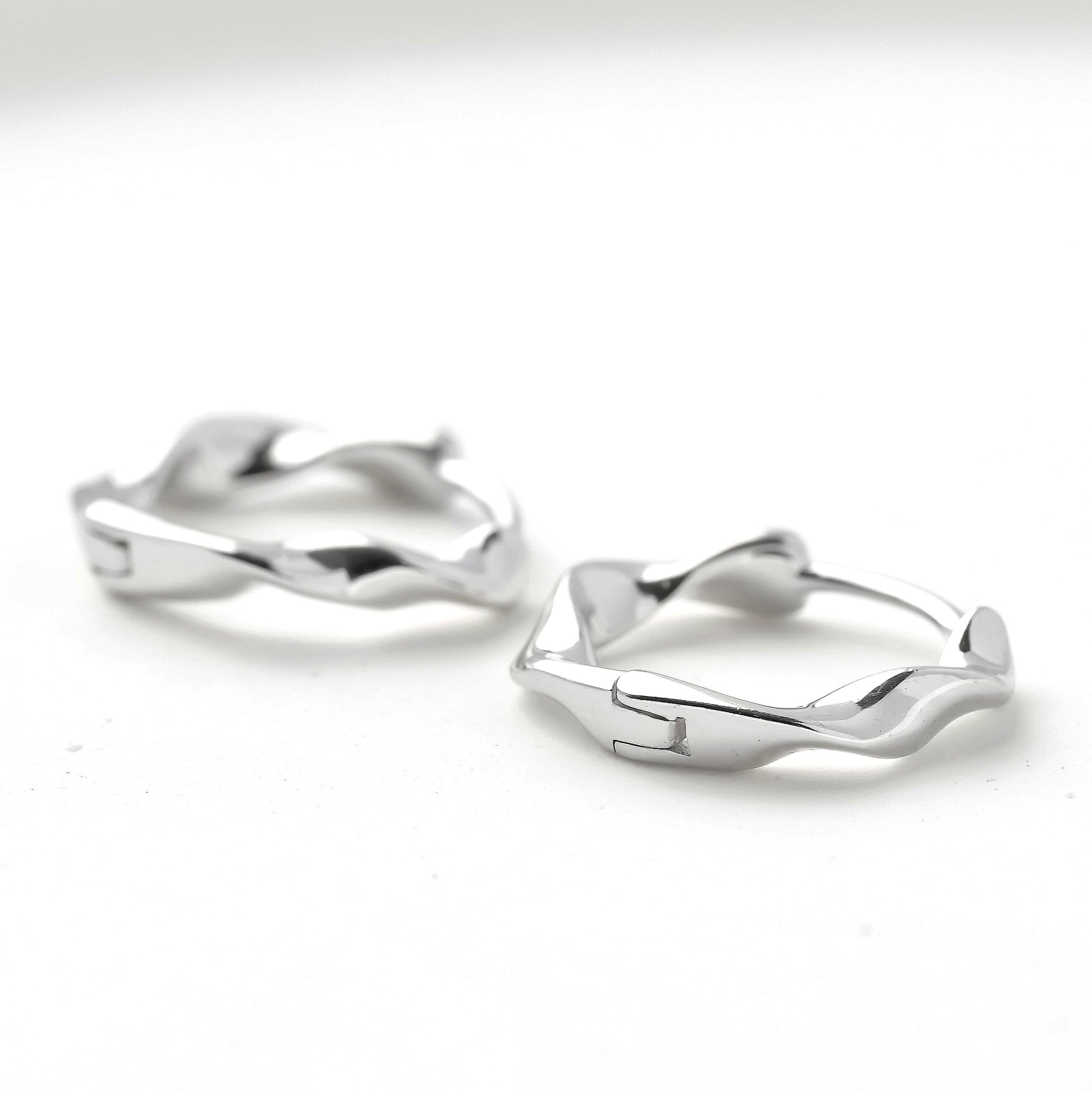 Pair of silver huggie earrings with hinged closure on a white background