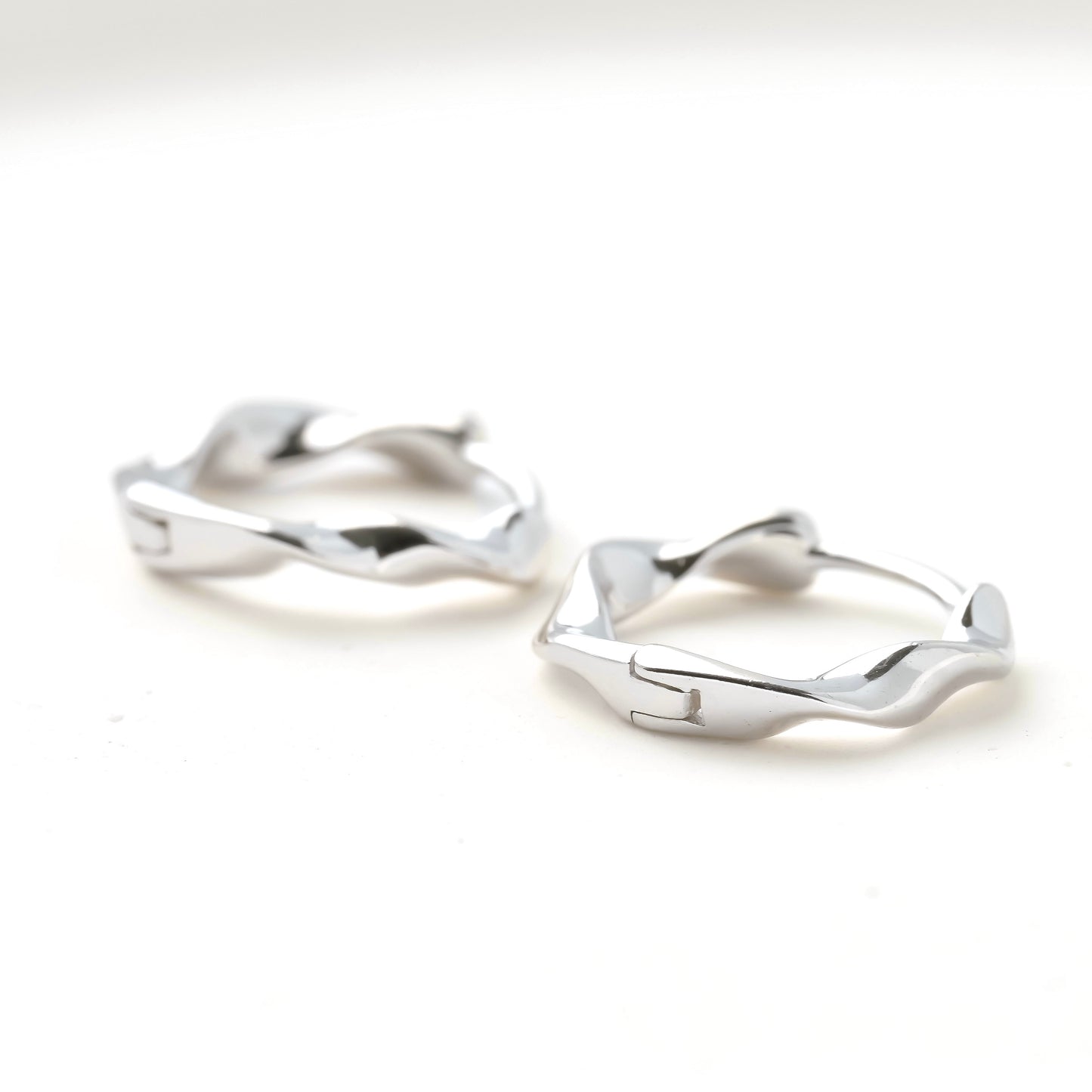 Pair of organic shaped twisted silver hoop earrings on a white background