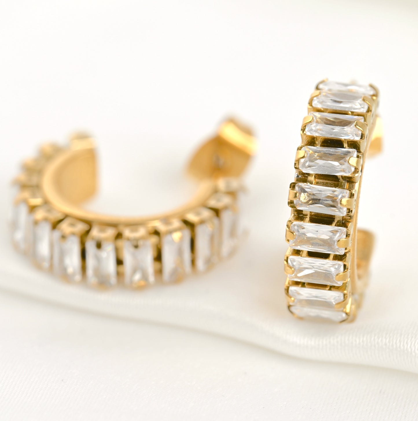 Gold baguette diamond hoop earrings with clear crystals on a white background