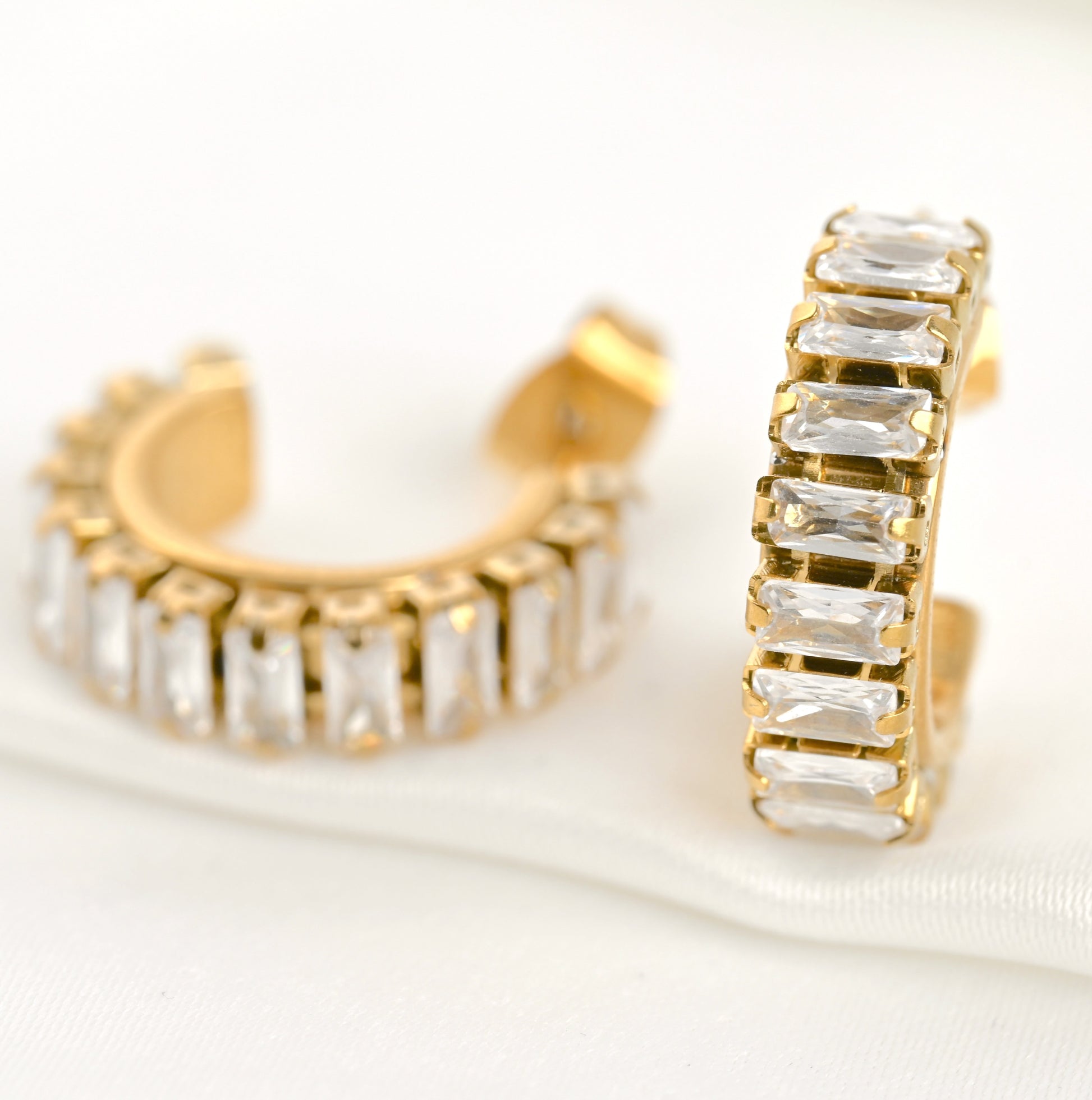 Gold baguette diamond hoop earrings with clear crystals on a white background