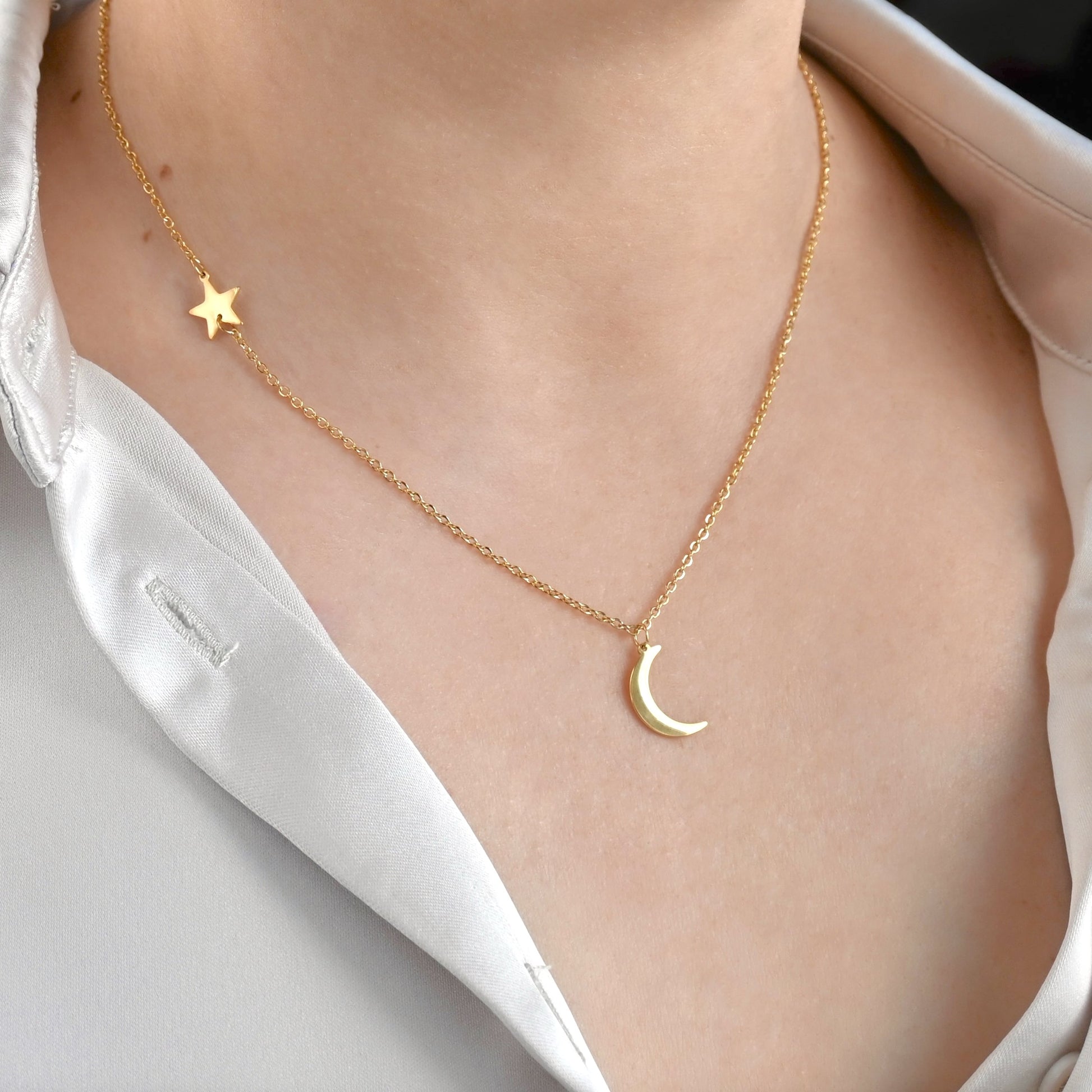 Gold necklace with star and crescent moon pendants on a person wearing a white shirt.