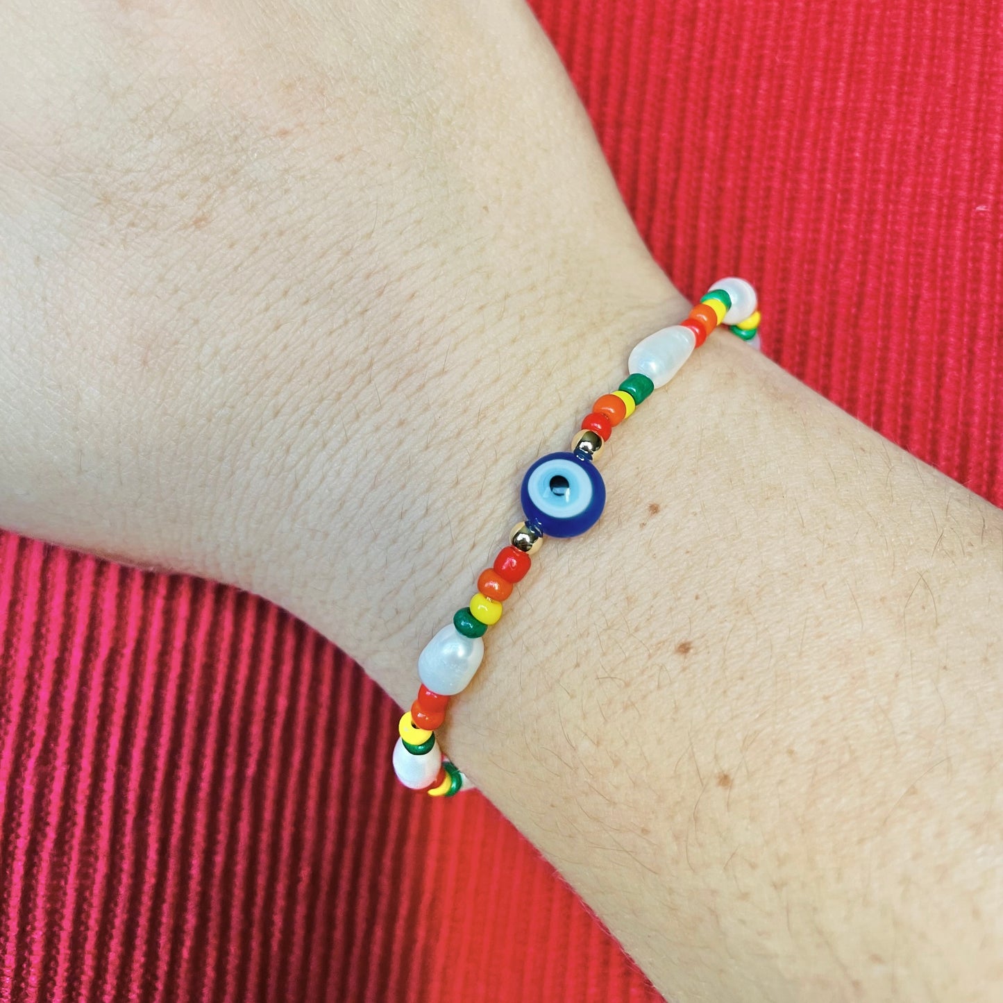 Colorful bead bracelet with natural pearls and  a blue eye charm on a wrist against a red fabric background