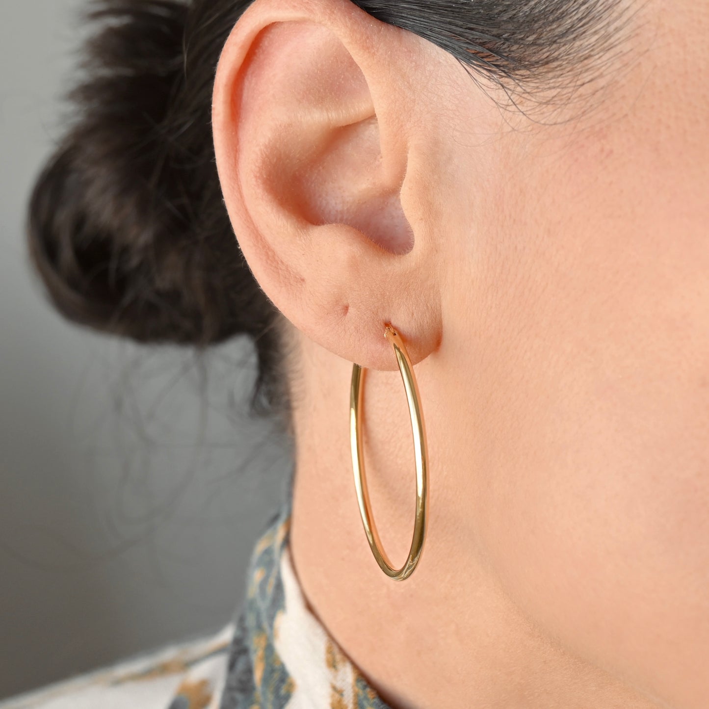 A close-up of a person's ear wearing slim, polished gold hoop earrings.