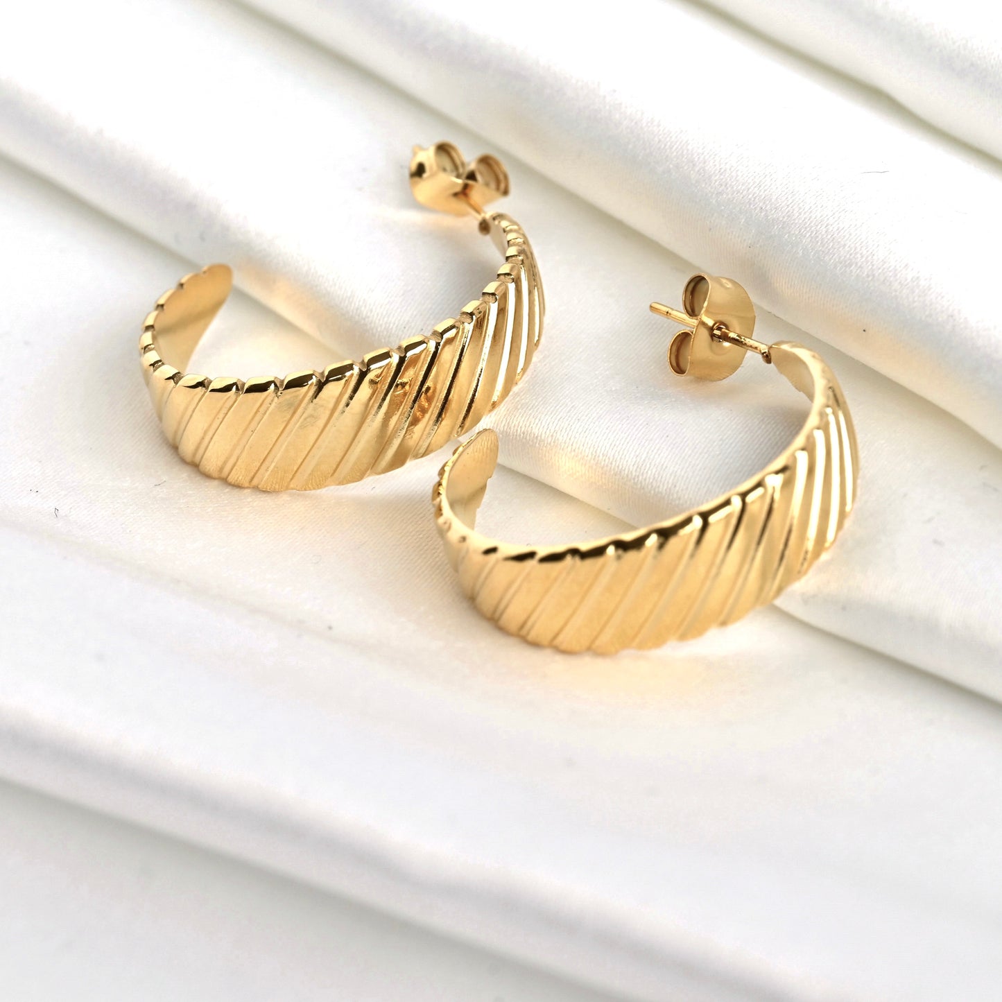 Tapered gold croissant hoops with push back closure on a white surface