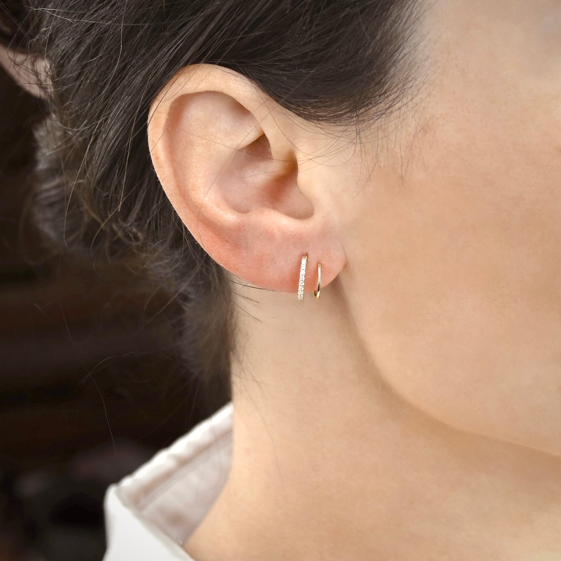 Close-up of an ear wearing gold hoop earrings with a blurred background
