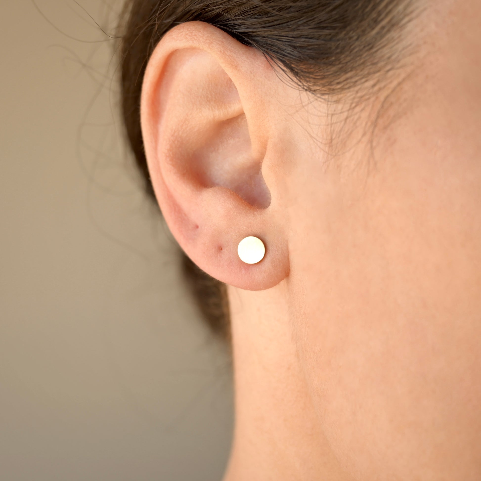 Close-up of an ear wearing small round filled circle earrings against a neutral background