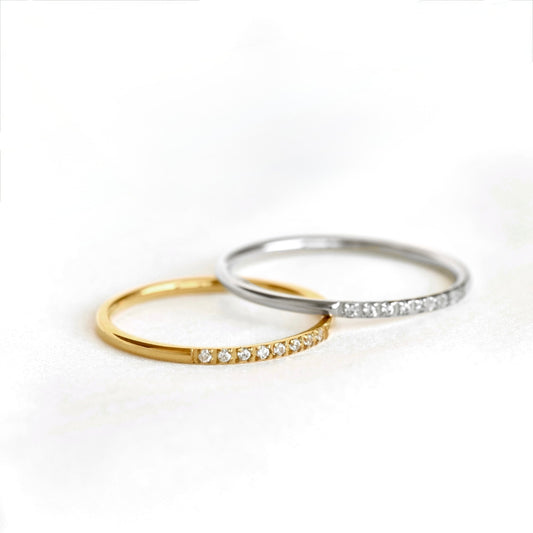 Two slim rings on a white background: one gold and one silver band both with a row of small clear stones in the front.