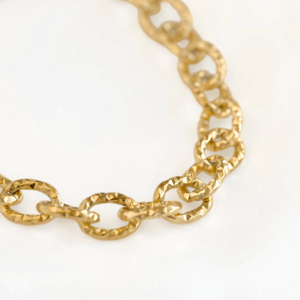 A close-up of a gold chain link bracelet with textured, faceted oval links on a plain white background.
