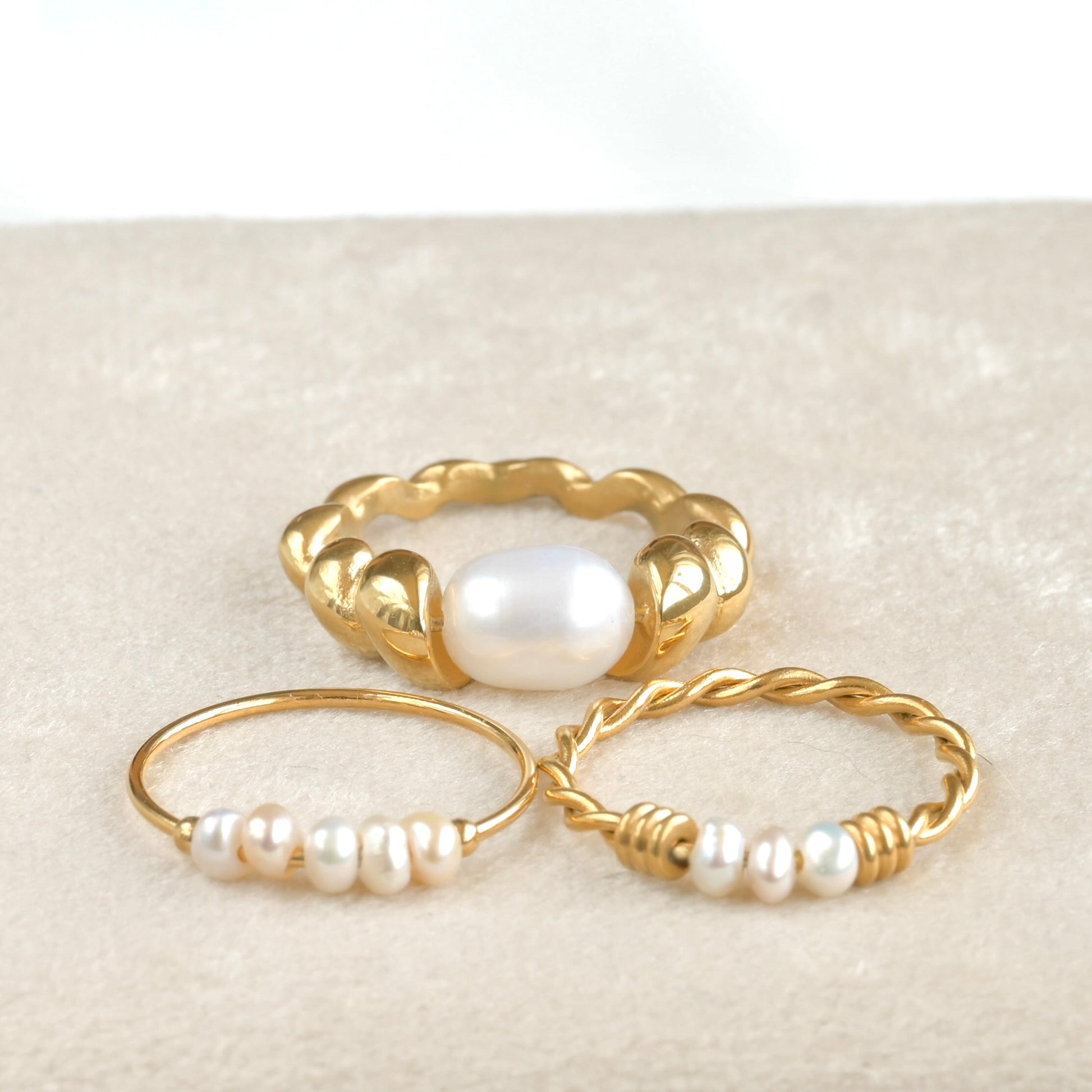 Three gold rings with pearls on a textured beige surface