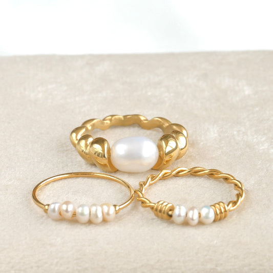 Three gold rings with pearls on a textured beige surface