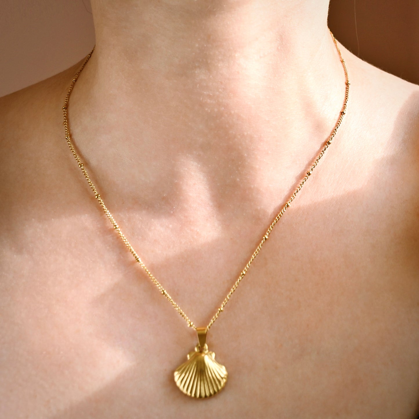 Front view of a gold chain necklace with a scallop shell pendant worn on a model's neck and upper chest.