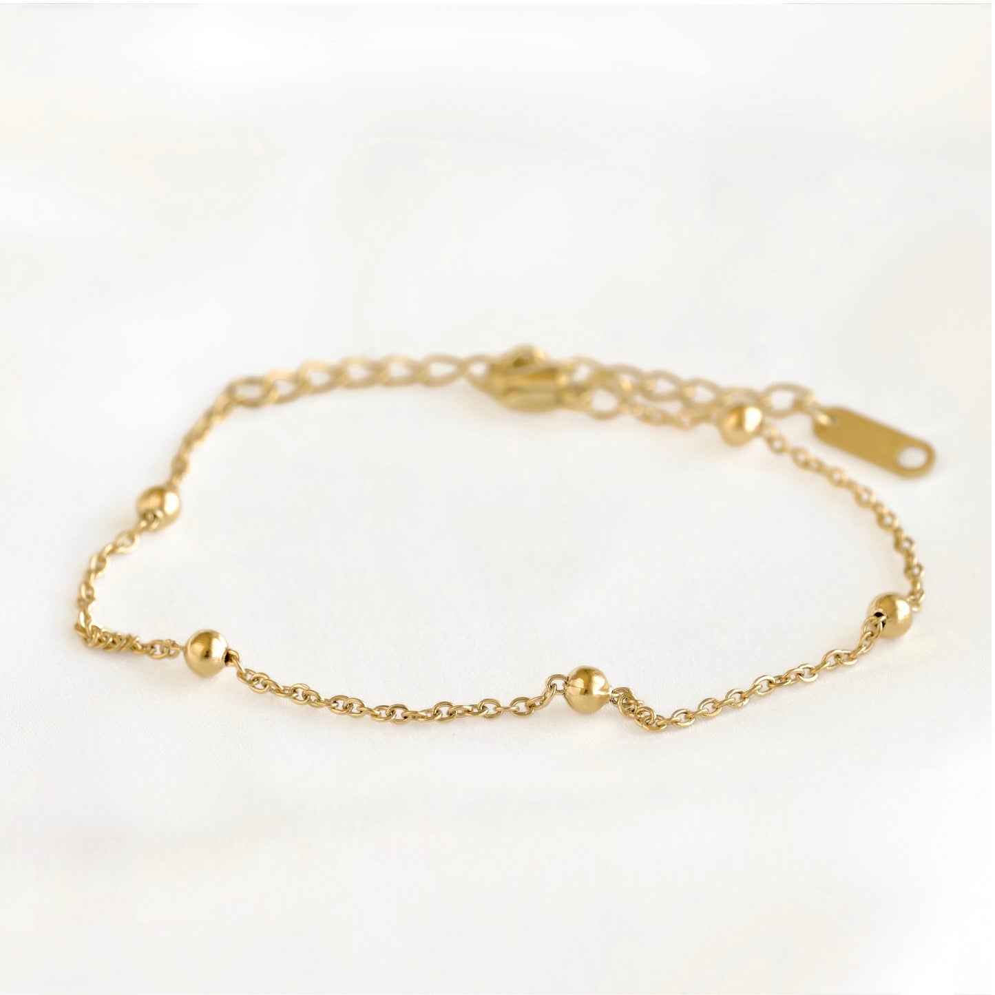 A delicate gold chain bracelet with small polished gold bead accents, displayed on a soft white background.