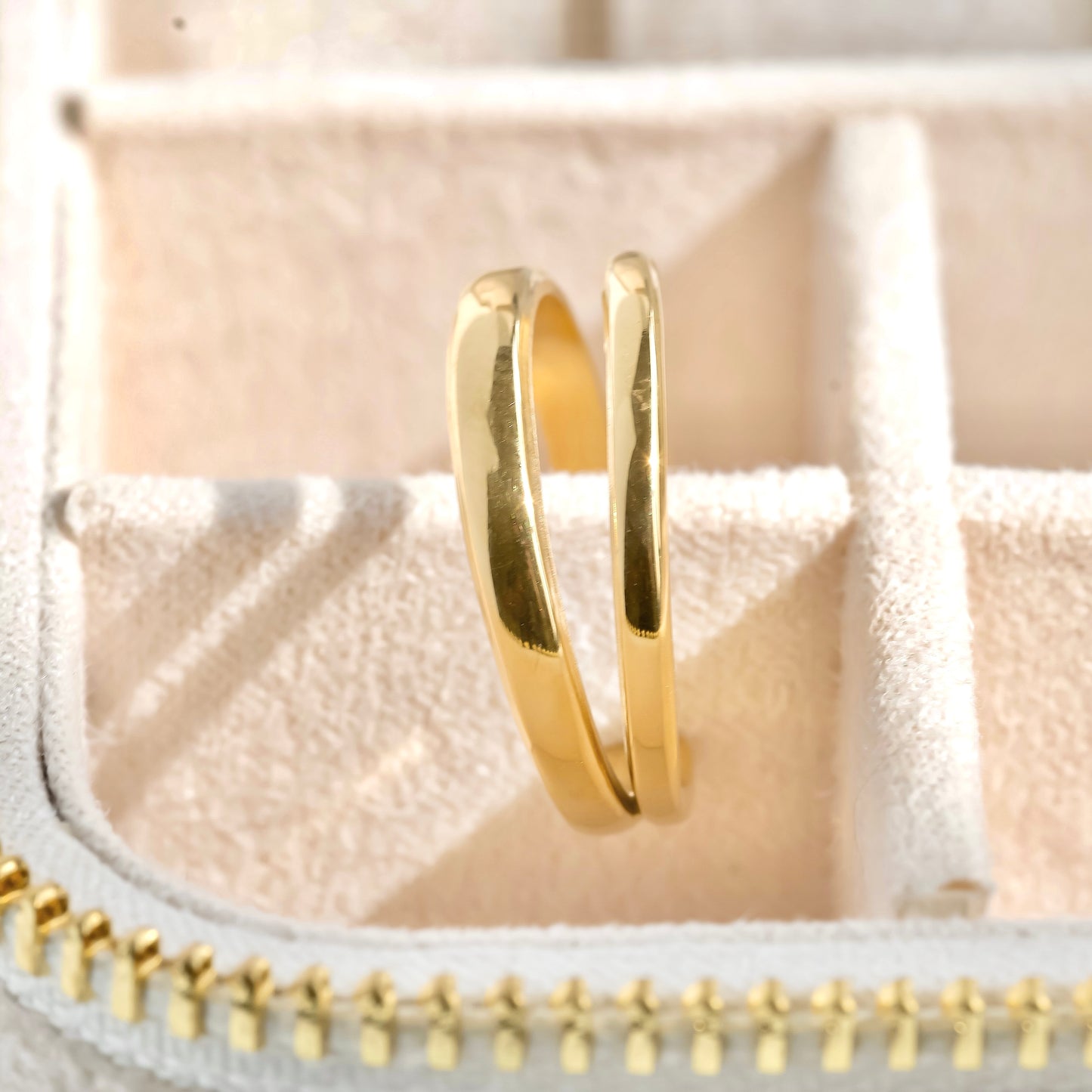 Gold ring with one thin and one thicker band on a textured beige surface under direct sunlight