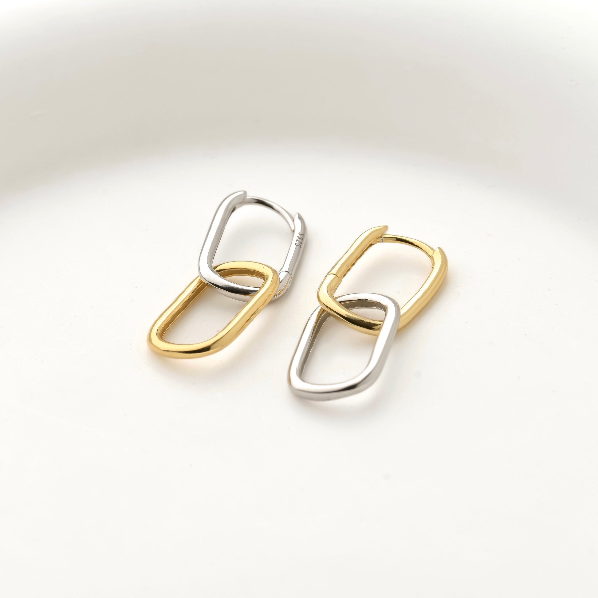 asymmetrical two-tone link chain earrings on a light gray background