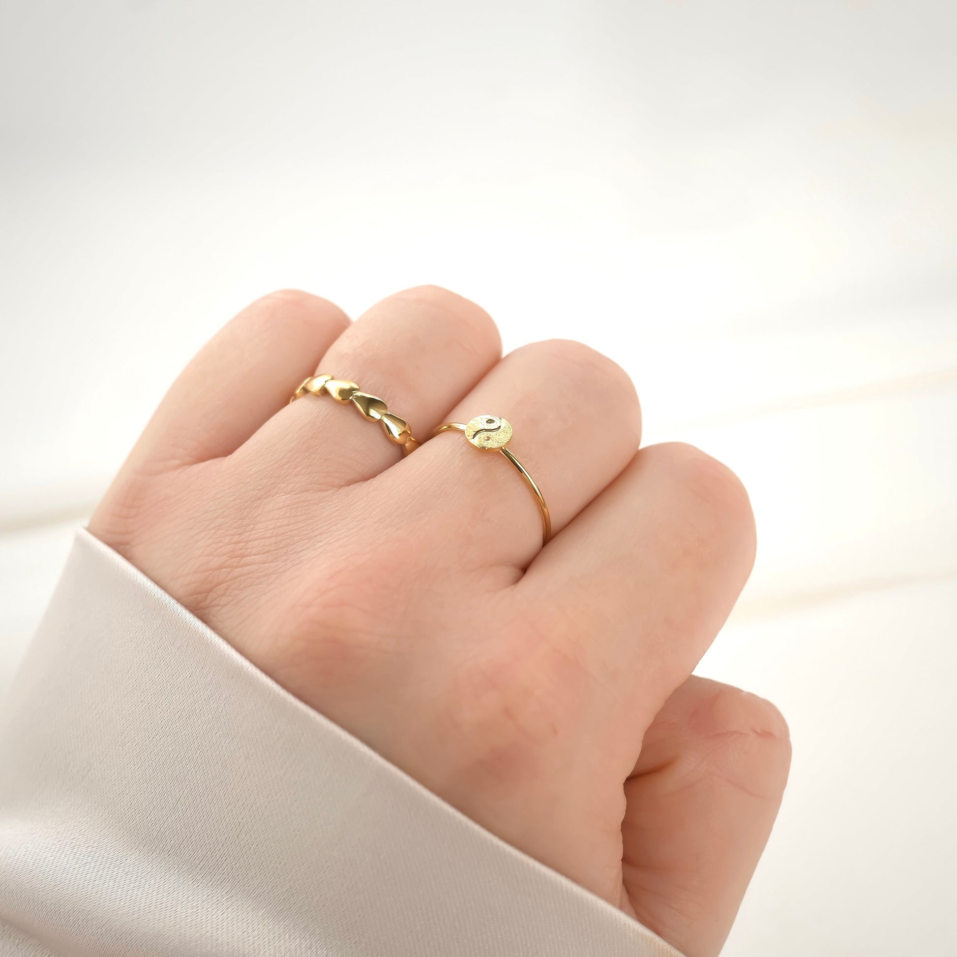 Gold taijitu ring on a finger against a white background