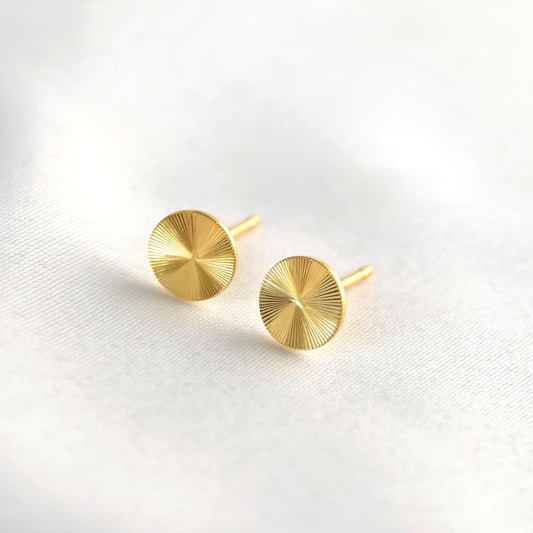 Pair of gold sun stud earrings on a light gray background