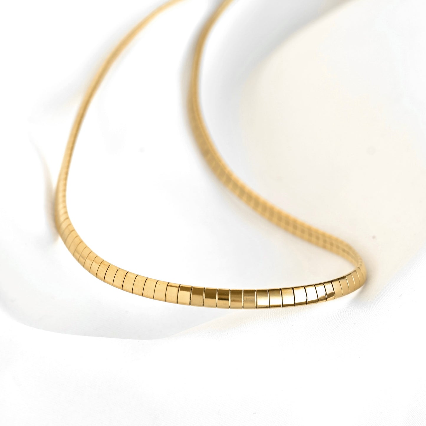 A close-up of a gold snake chain necklace resting on a white surface.